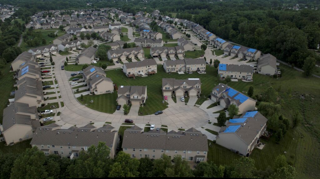 Bird's eye view of a residential neighborhood with tarps on various roofs that are being repaired.