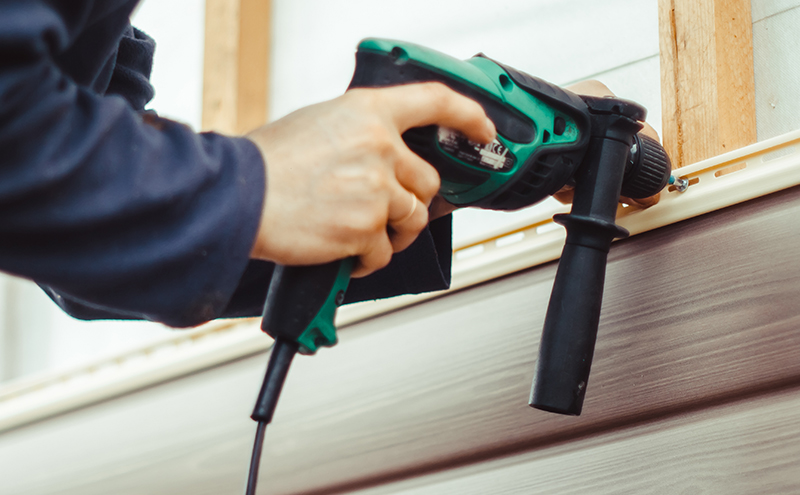 Close up of man installing siding with drill.