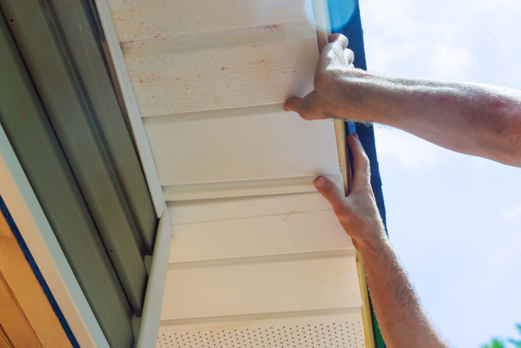 A man's hands installing soffit plastic panels.